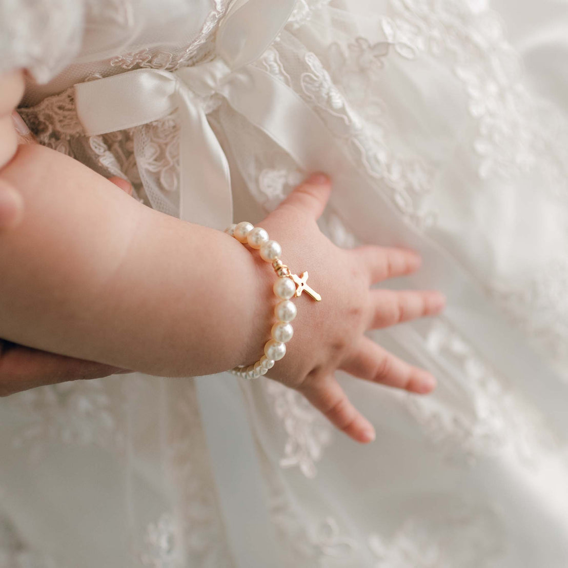 Baby girl wearing the Cream Luster Pearl Bracelet with Gold Cross. Made with cream color Swarvoski pearls, gold plated beads and gold plated clasp.