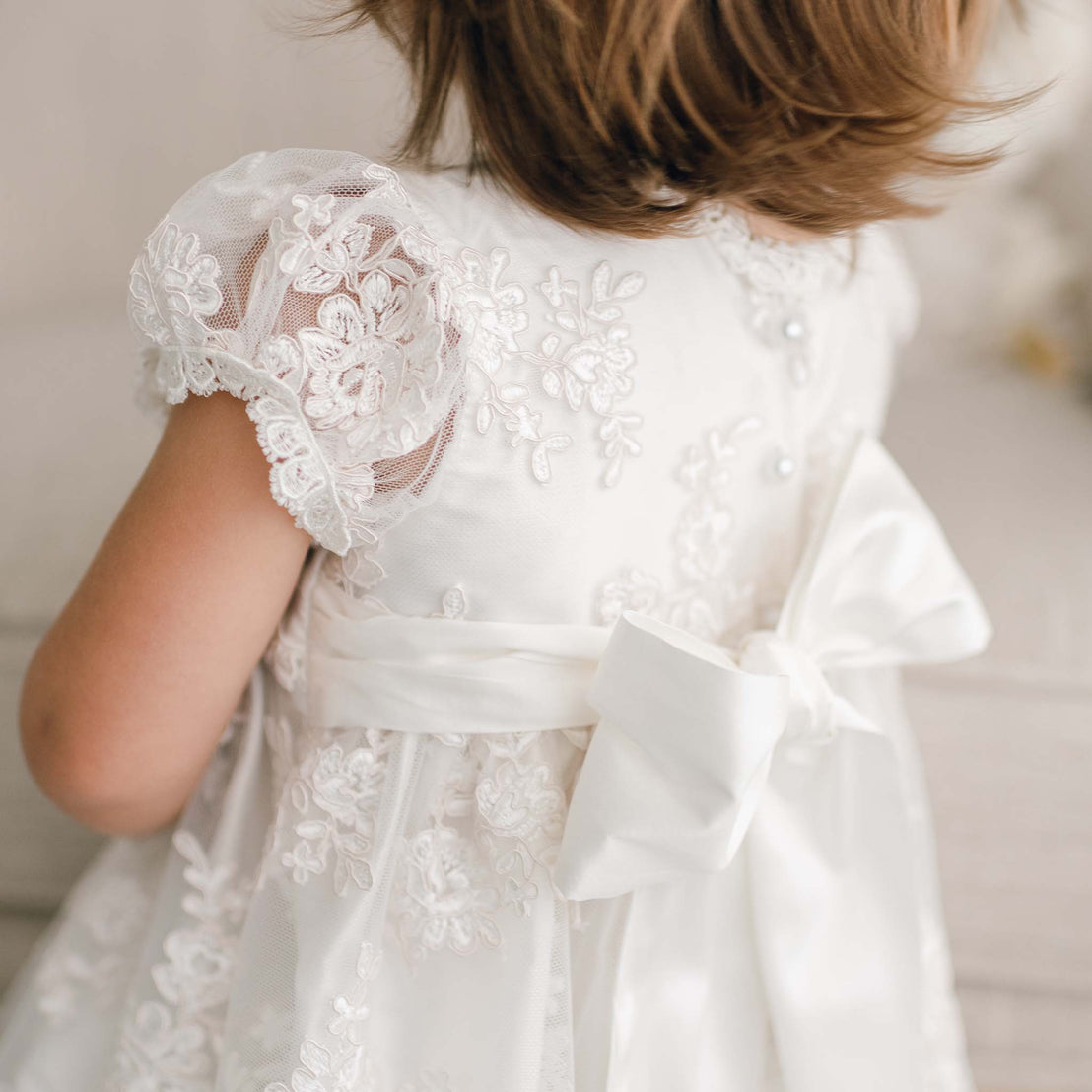 Close up detail of the bow on the back of the Penelope lace christening dress.