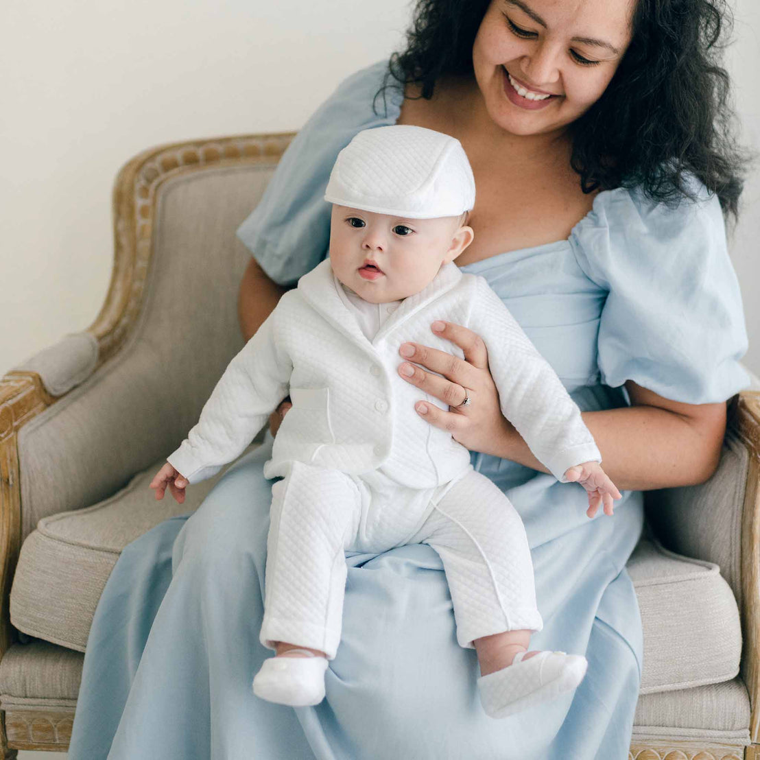 Baby boy sitting with his mother and wearing the Elijah 3-Piece Suit made from 100% white textured cotton jacket and pants, and a white cotton / rayon blend shirt.
