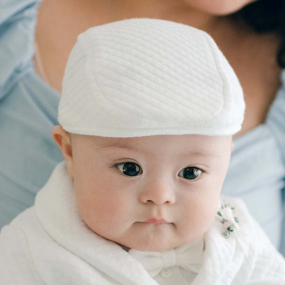 Baby boy sitting on his mother's lap and wearing the Elijah Newsboy Cap. The photo features the top of the hat in the "newsboy" style in a white textured cotton.