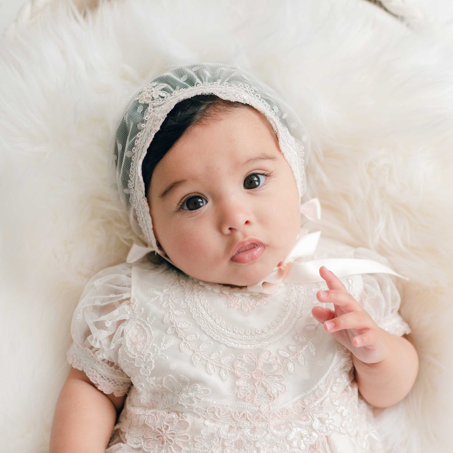 Close-up of a baby in the Elizabeth Newborn Christening Bonnet, featuring the ivory and pink edge laces along the front of the sheer bonnet.