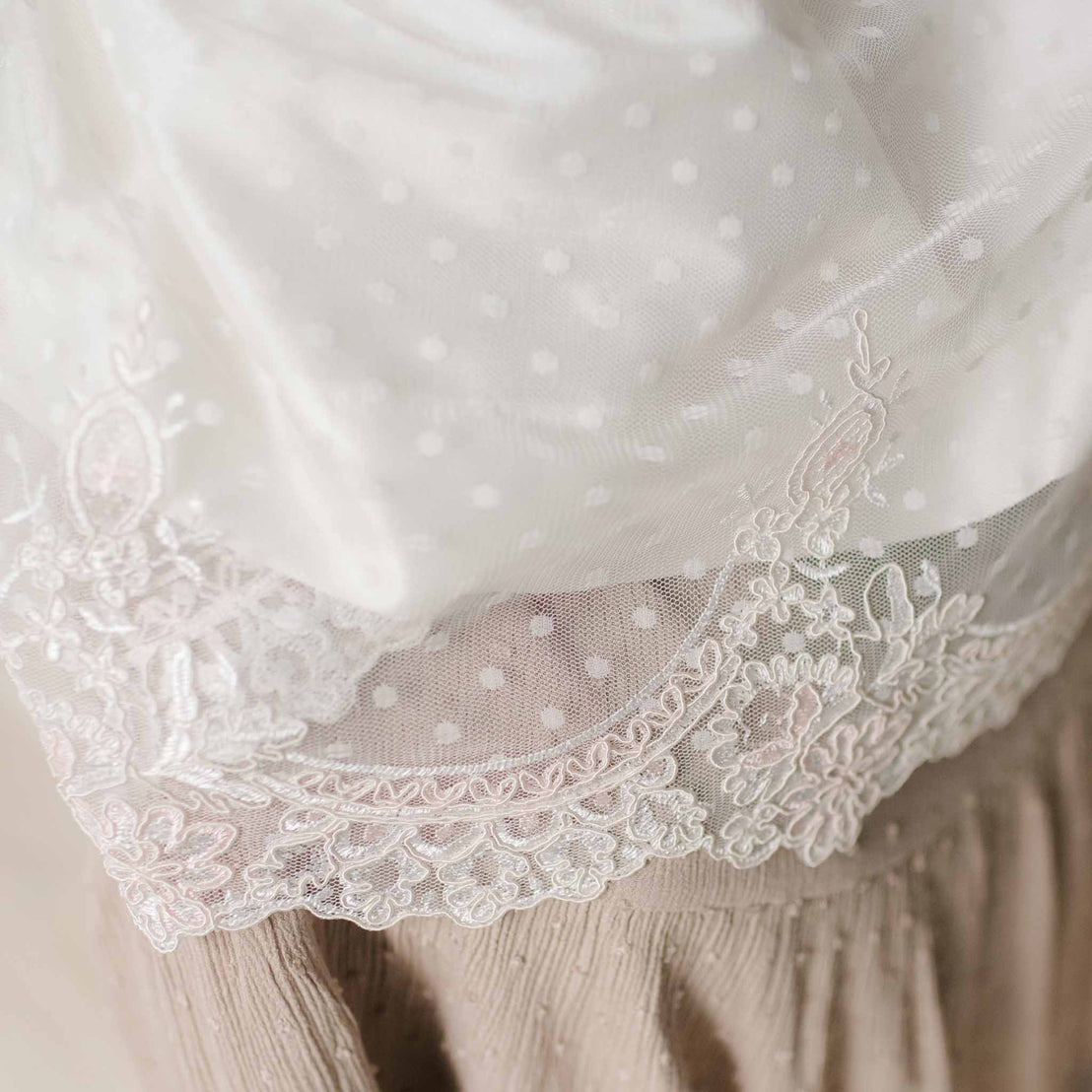 Close-up of the scalloped lace at the hem of the skirt on the Elizabeth Newborn Christening Dress set against a neutral background. 