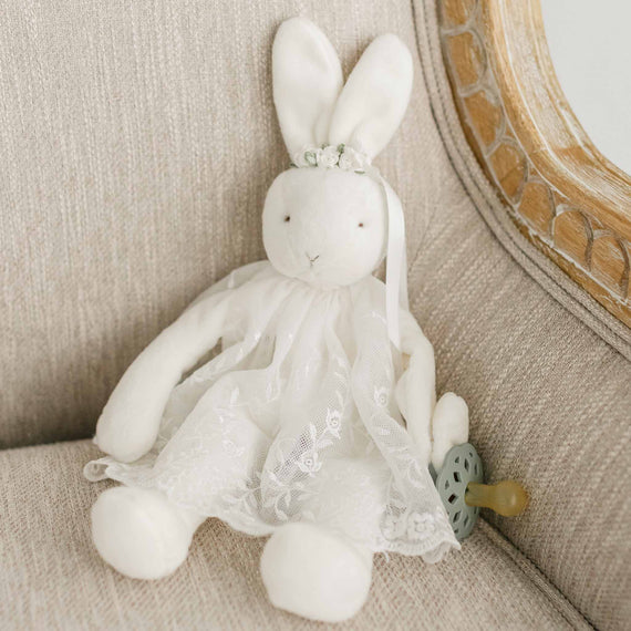 A flat lay photo of the Ella Silly Bunny Buddy dressed in a mini Ella Lace baptism dress and floral headband.