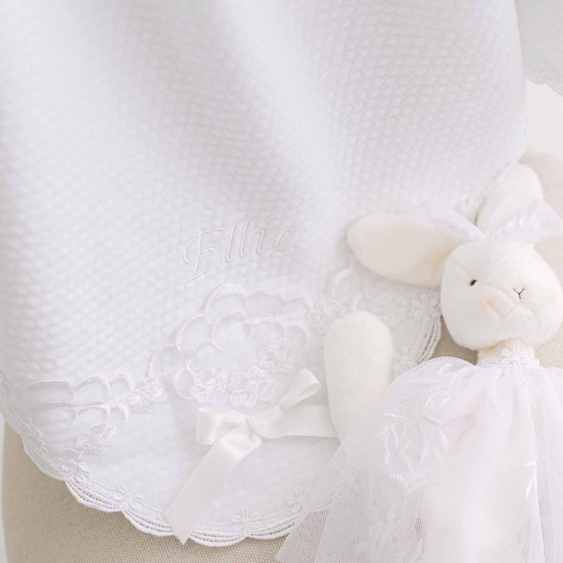 White quilt blanket with a white plush bunny toy on a neutral background