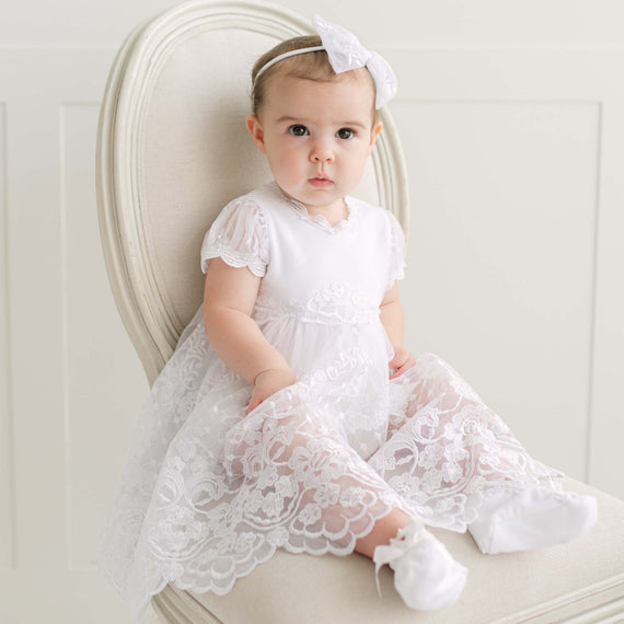 Baby in a white lace dress sitting on a beige chair