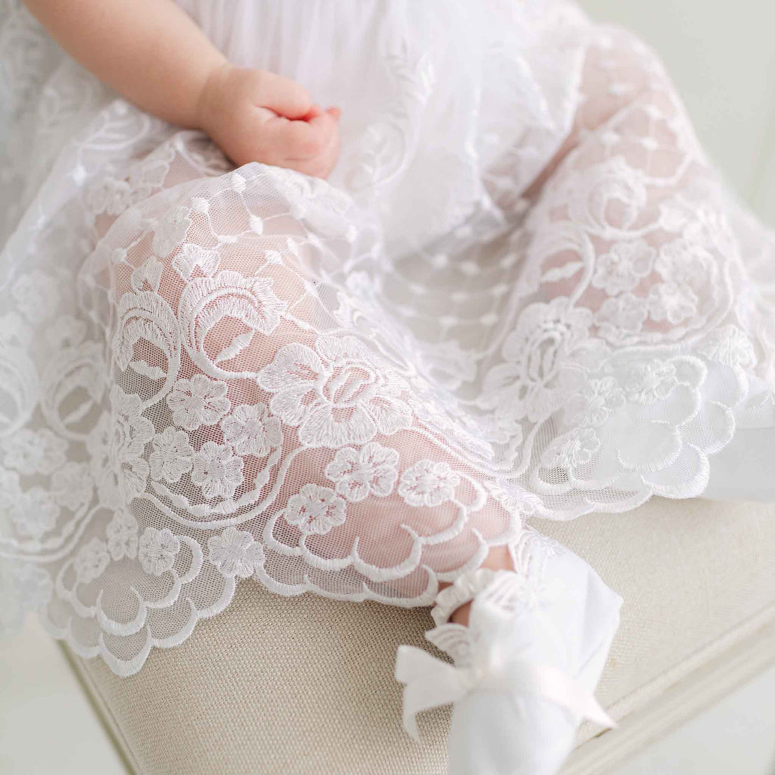 Close-up of a baby's legs in a white lace skirt on a beige chair