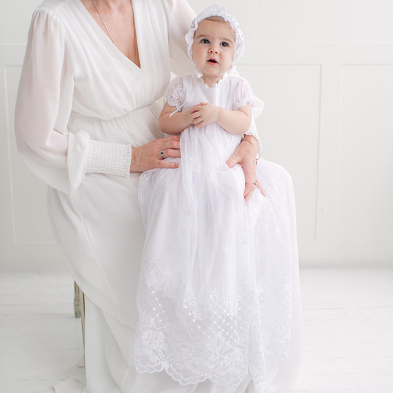 Woman holding a baby dressed in white gown against a white background