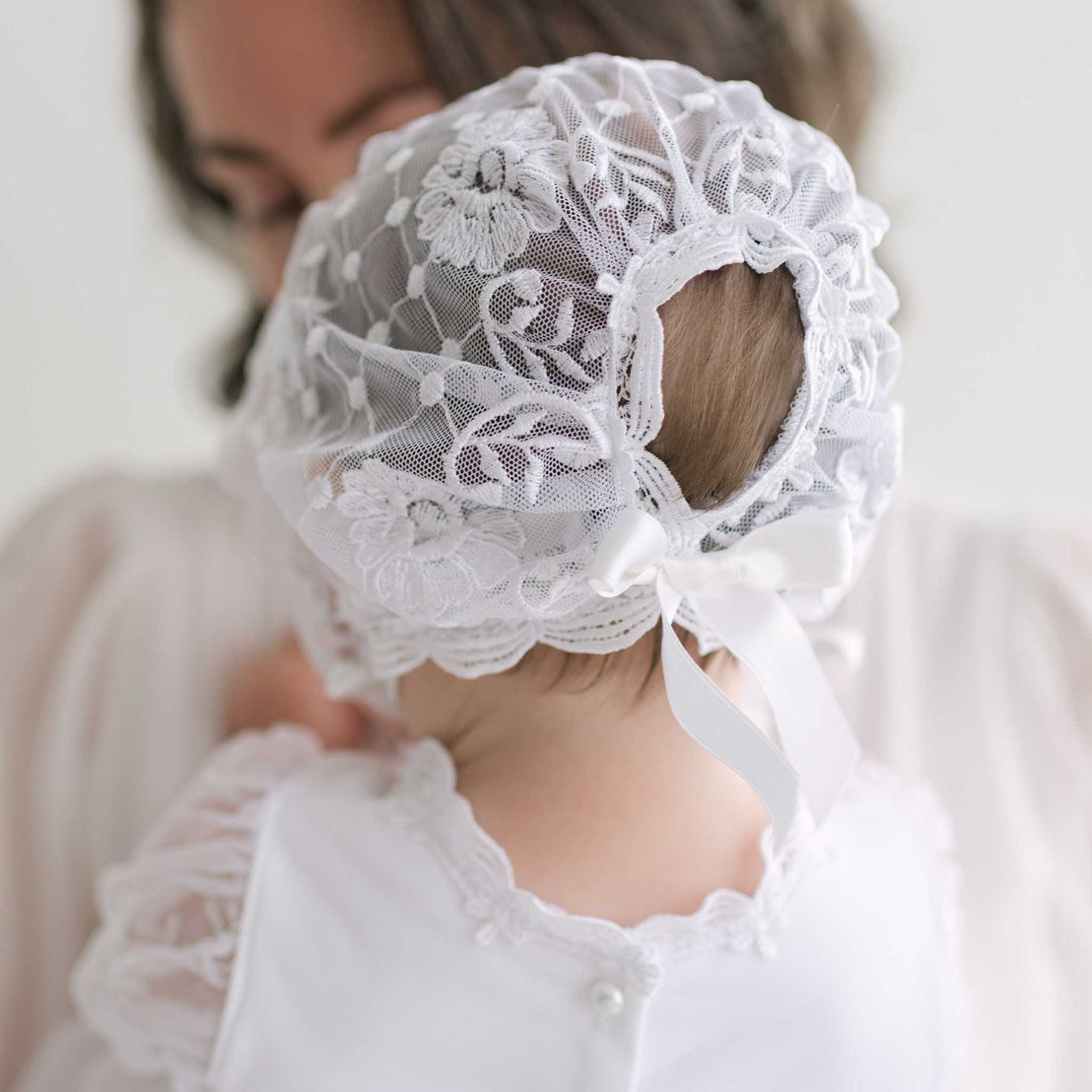 Baby wearing a white lace bonnet with a blurred background