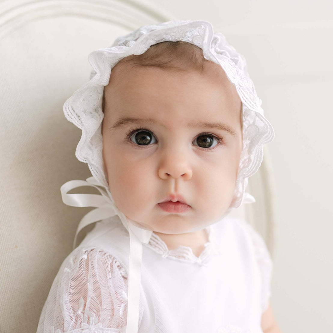 Baby wearing a white bonnet against a neutral background