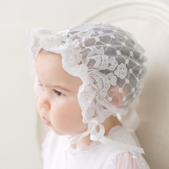 Baby wearing a lace bonnet against a neutral background