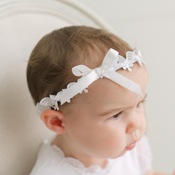 Baby wearing a white lace headband with a neutral background