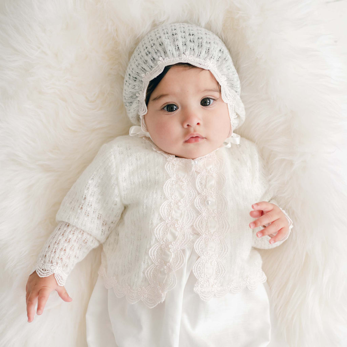 Baby wearing a white knitted sweater and bonnet on a soft white background