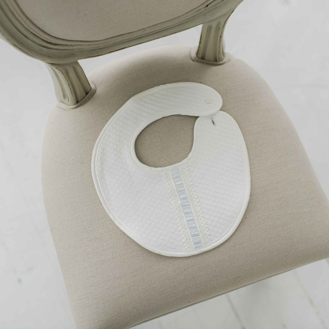 White bib with blue lace on a beige chair