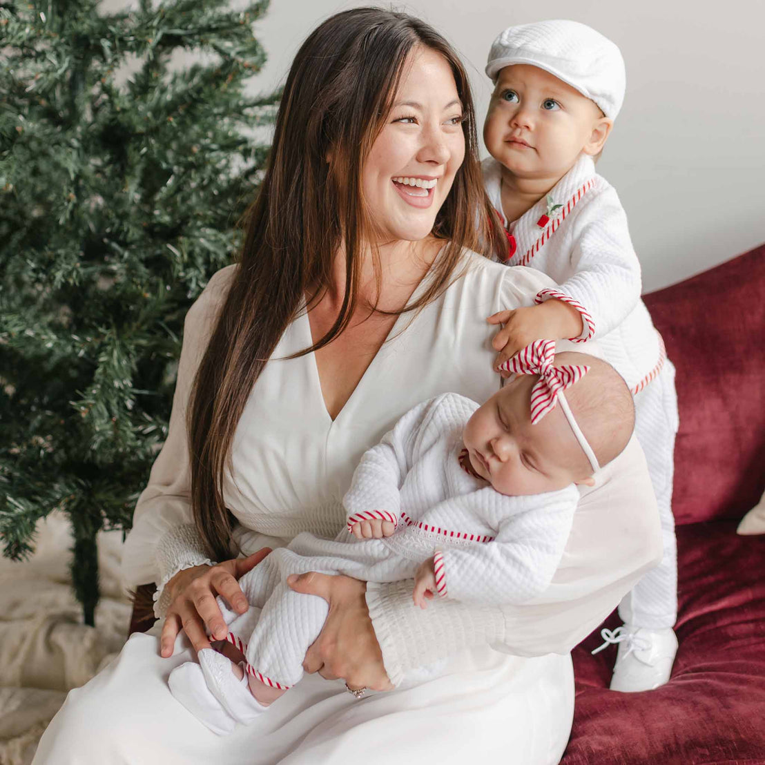 Woman holding two babies in front of a Christmas tree