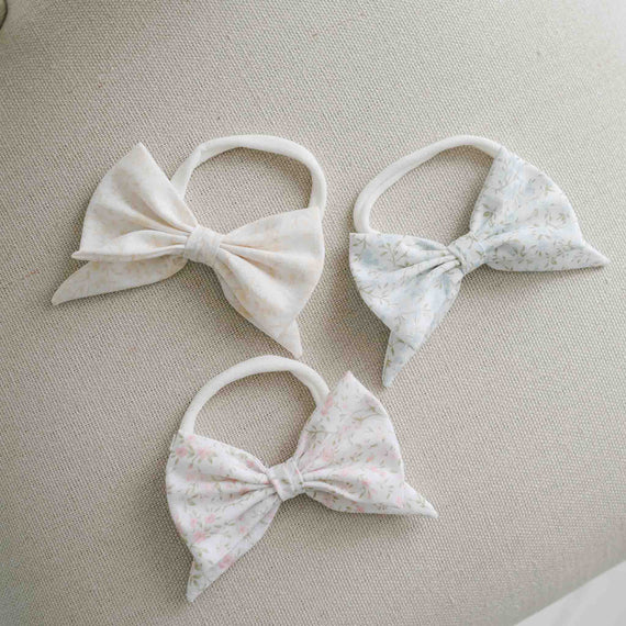 Three linen bow headbands with a floral pattern on a beige surface