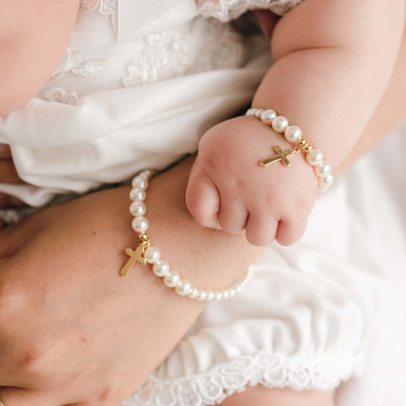Close-up of a hand and child's hand wearing pearl bracelets with gold crosses.