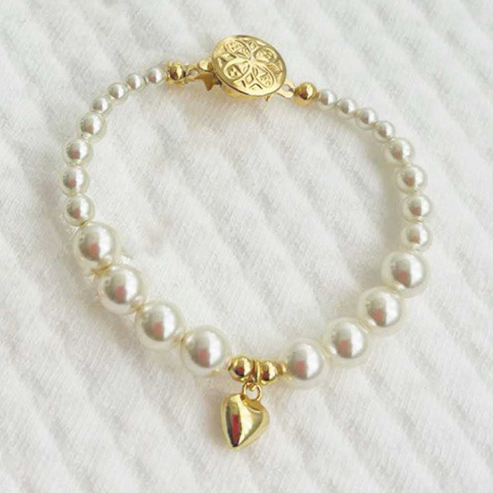 Cream pearl baby bracelet with gold plated heart charm on a white textured background