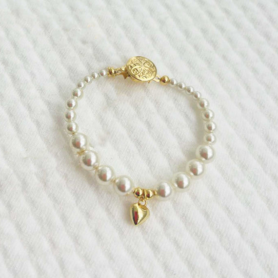 Cream pearl baby bracelet with gold plated heart charm on a white textured background