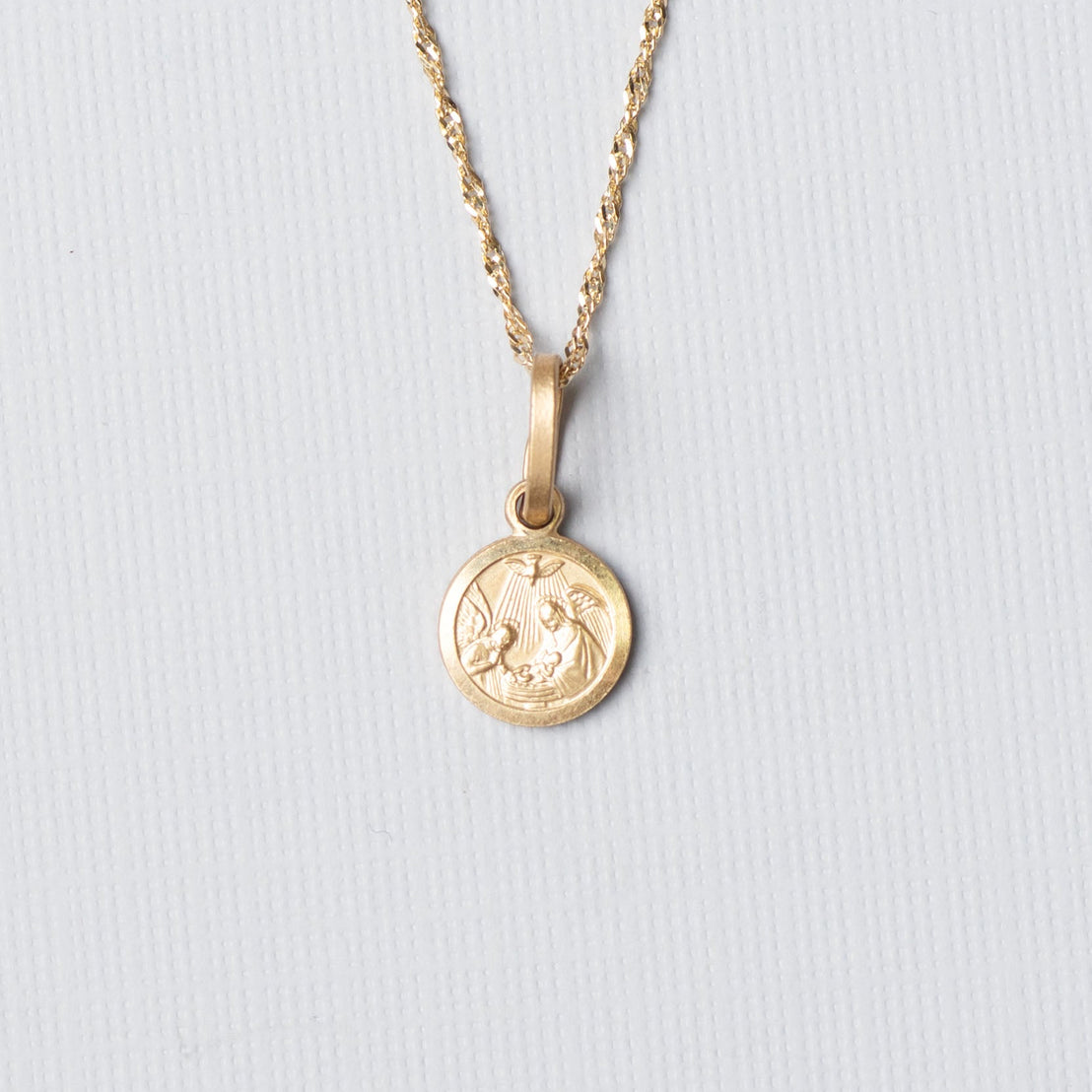 Gold necklace with a round pendant on a light gray background