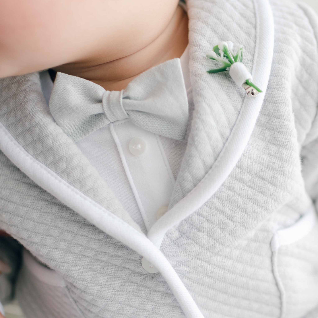 Close-up of a baby in a white outfit with a bow tie and a green toy.