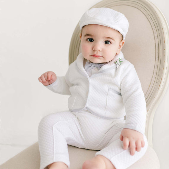Infant wearing the Harrison Christening Pants Suit, styled with a white quilted jacket, pale blue trim, matching pants, a bow tie, and a classic cap.