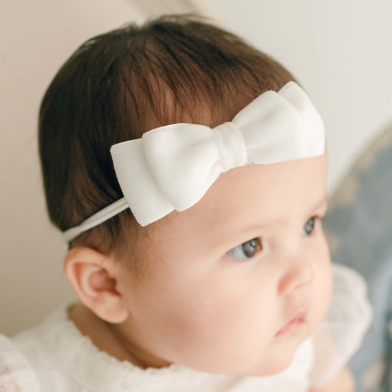 A newborn baby girl wearing the Ella Baby Girl Bow in Velvet looks away from the camera. 