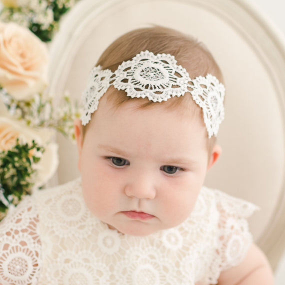 Baby girl wearing large lace christening headband on head.