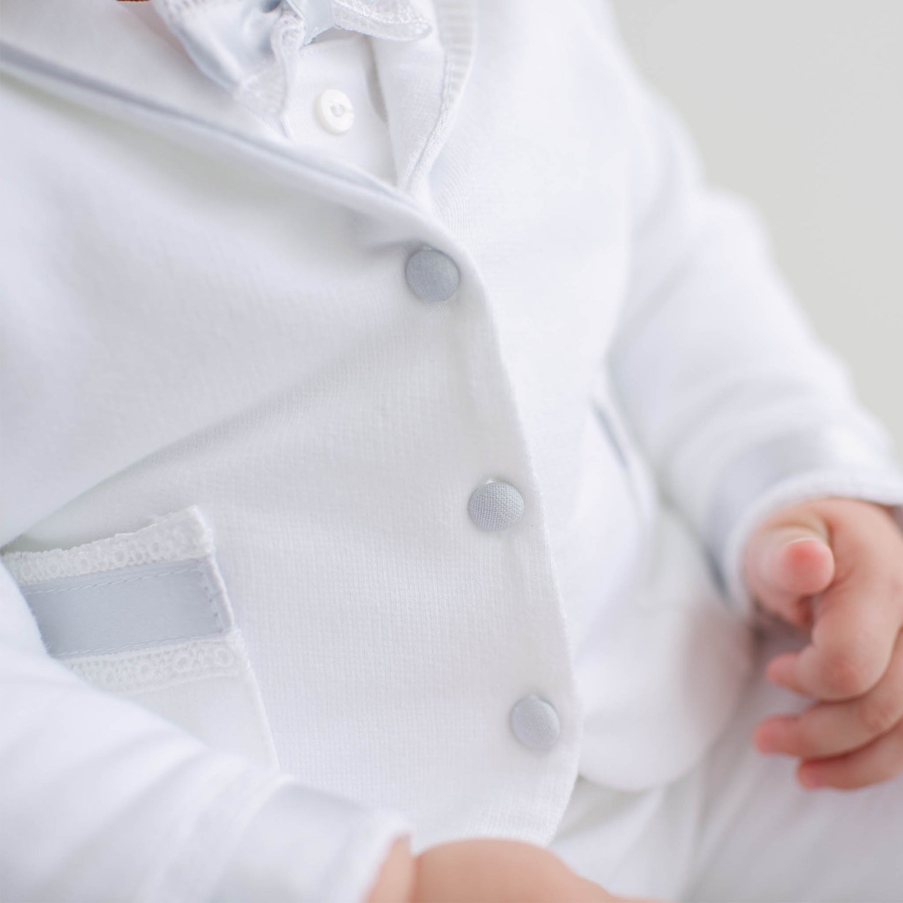 Close-up of a baby in the Henry 3-Piece Suit. Details show blue linen buttons and Venice lace and silk ribbon detailing.