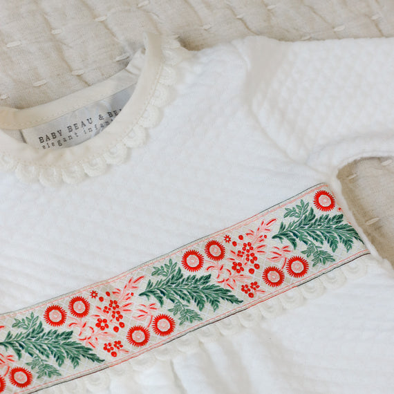 White quilt baby romper with festive floral trim on a beige background