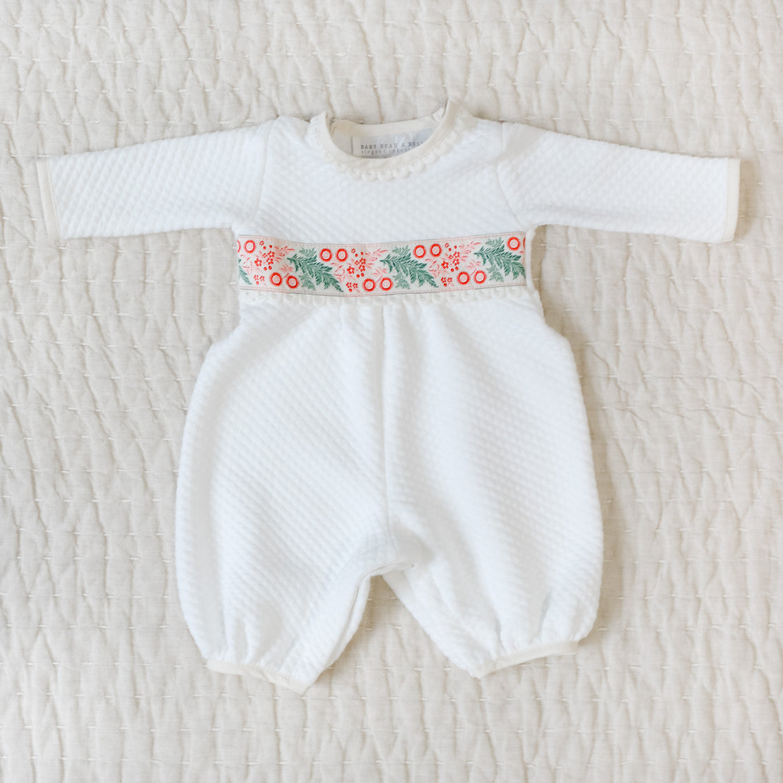 White baby romper with festive waistband on a textured beige surface