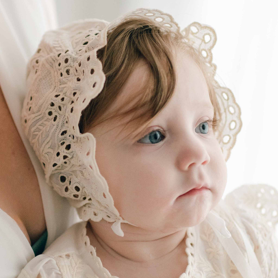 Baby wearing the Ingrid Lace Bonnet crafted with a 100% cotton lace in light ivory and a natural champagne tone