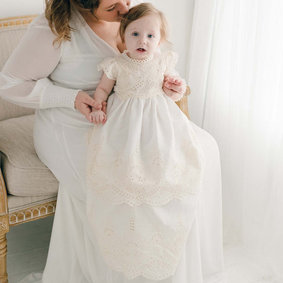 Baby girl wearing an Ingrid cotton blessing gown in ivory and sitting on mother's lap 