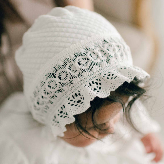 Baby wearing the Lily Quilted Cotton Bonnet made with ivory quilted cotton, light ivory stretch lace, and light ivory cotton ribbon