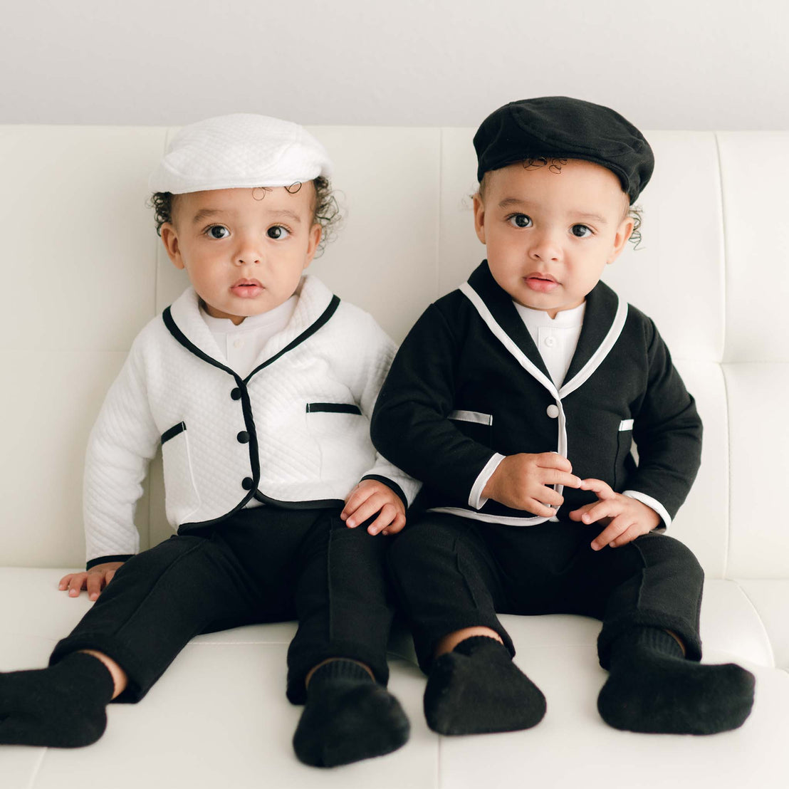 Two twin boys sitting on a couch and wearing the James 3-Piece Suits. One boy is wearing the white jacket and the other is wearing a black jacket.. The 3-Piece Suit includes the jacket, pants and onesie.