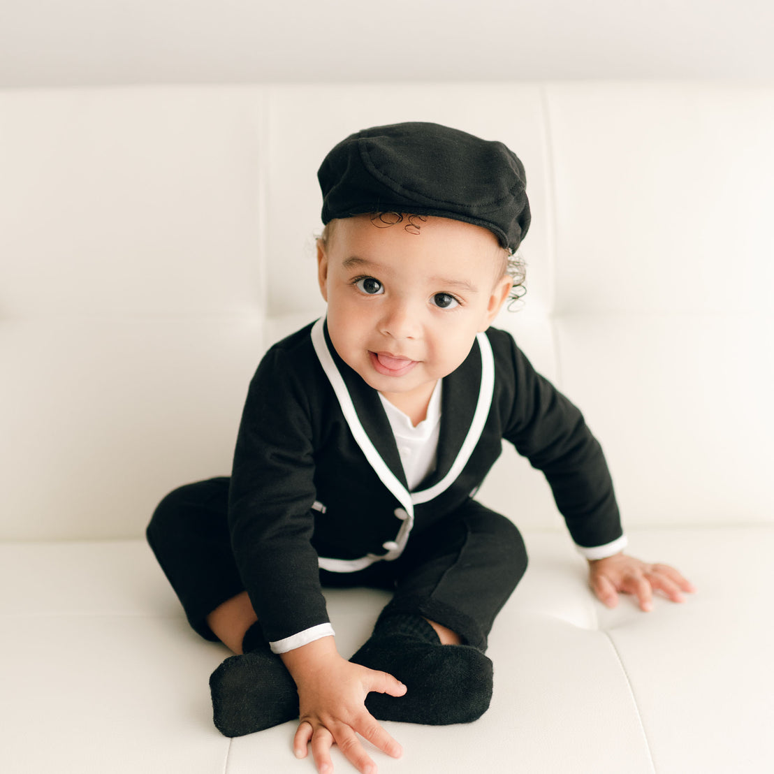 Baby boy sitting on a couch and wearing the black James 3-Piece Suit (and matching Newsboy Cap).