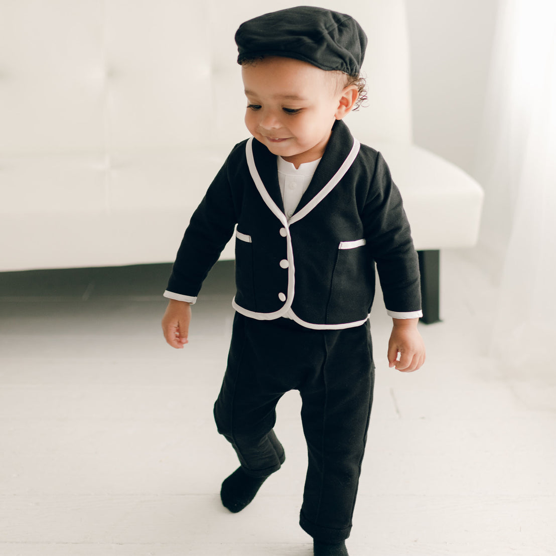 Baby boy standing up and wearing the black James 3-Piece Suit (and matching Newsboy Cap).