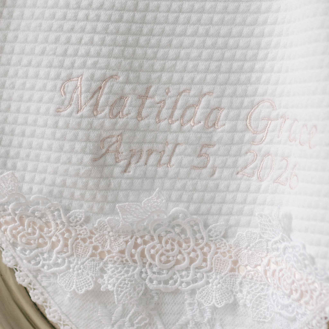 White quilt with pink embroidered text and white lace trim