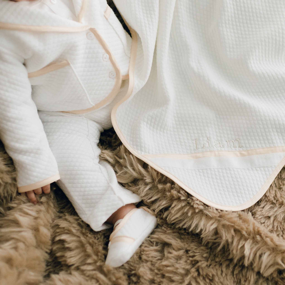 Photo of a baby sitting on a brown fur blanket. The baby is wearing the Liam 3-Piece Suit and is covered with the Liam Personalized Blanket