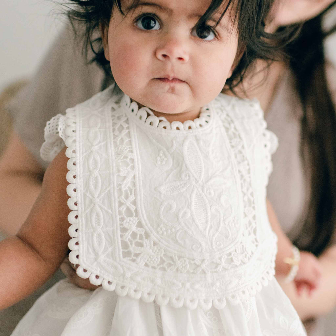 Baby wearing the Lily Lace Bib that is made out of cotton lace in light ivory and exhibits a unique squared design and circle lace trim