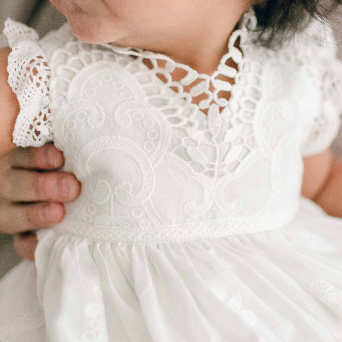 Detail of the top bodice of a christening romper dress worn by a baby girl