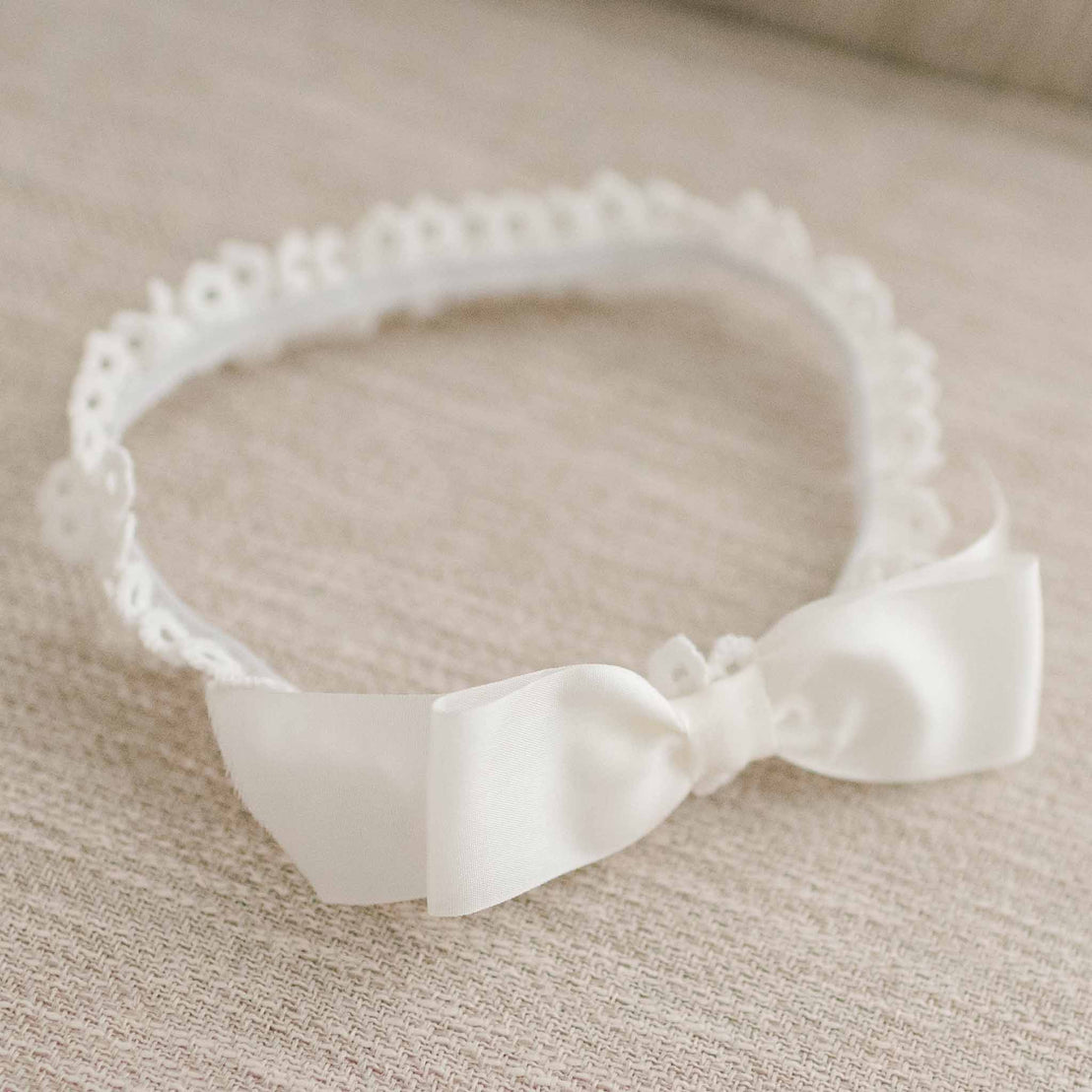 Flat lay photo of the Lily bow headband made of soft, cotton lace and featuring a silk ribbon bow