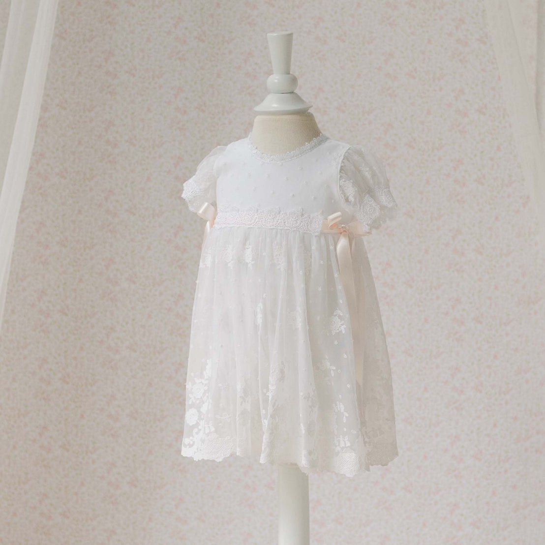 Full length view of the Melissa Romper Baby Girl Baptism Dress on a mannequin against a light background. Details show Swiss and floral border embroidered pattern netting and white Venice lace trims. Perfect for a baptism or baby blessing.