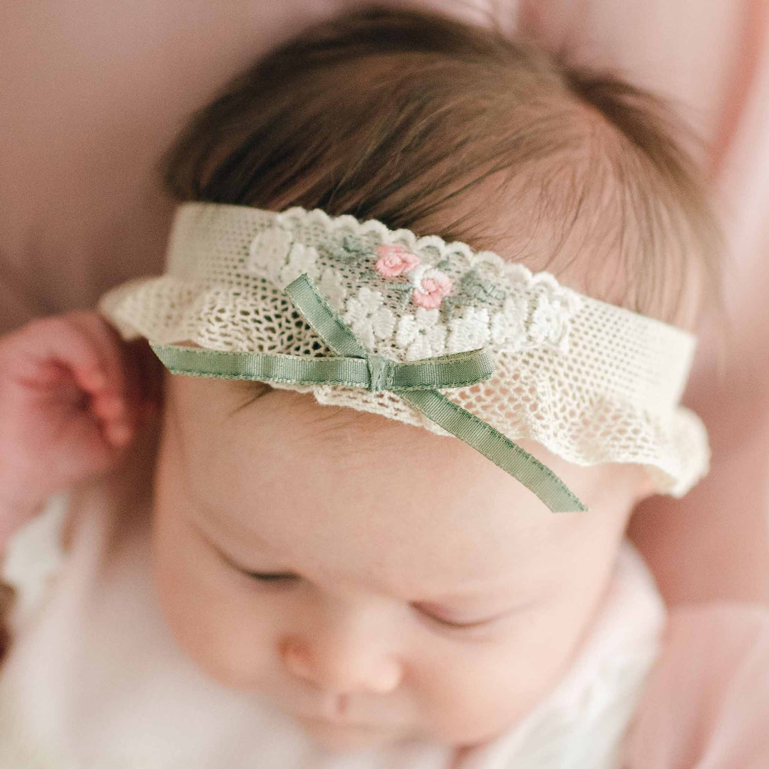Baby girl wearing a Natalie Headband made from cotton netting with a vintage natural cotton lace, pink rosettes, olive green leaves, and a green ribbon tie 