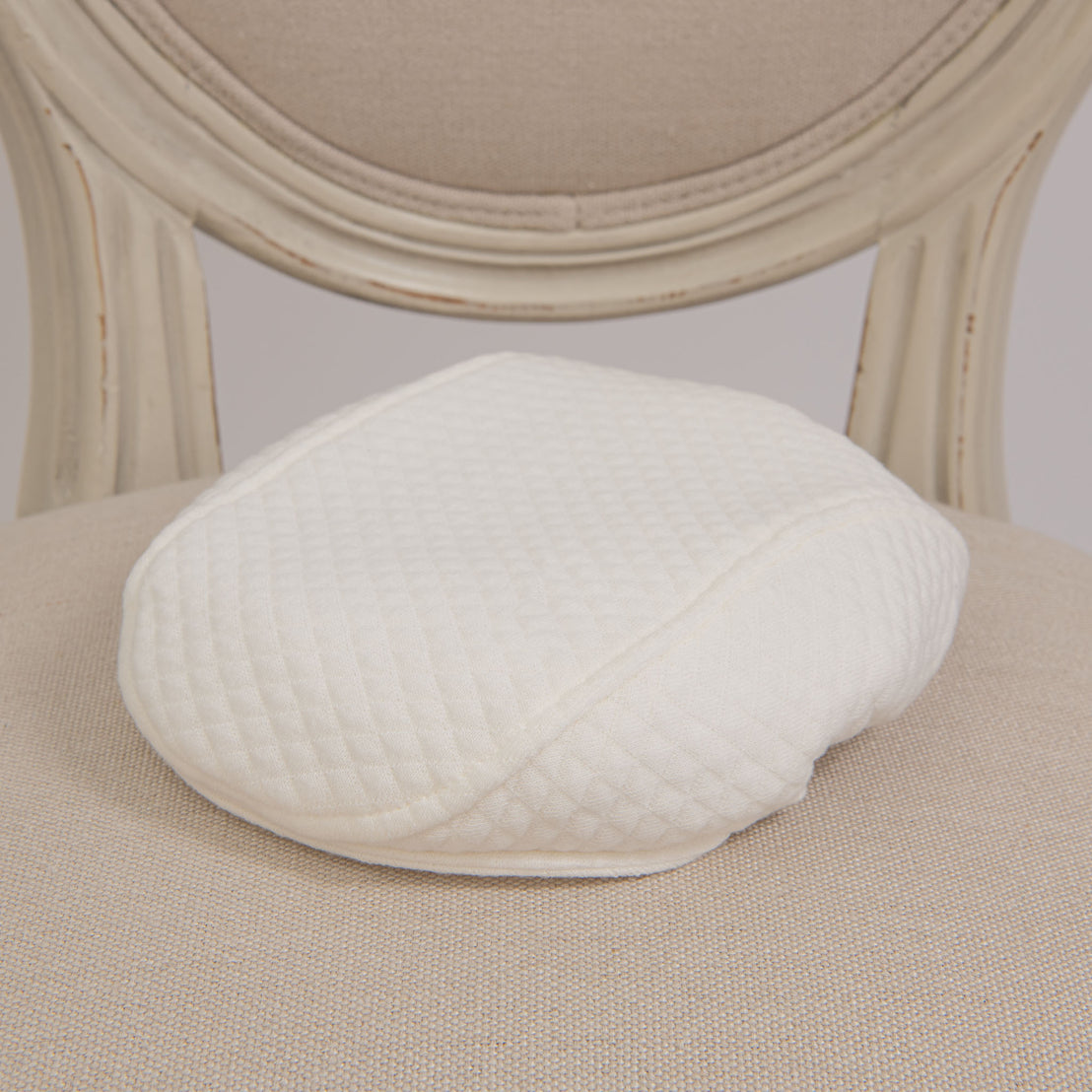 Flat lay photo of the Owen Cotton Newsboy Cap on a chair. The hat is made with ivory quilted cotton