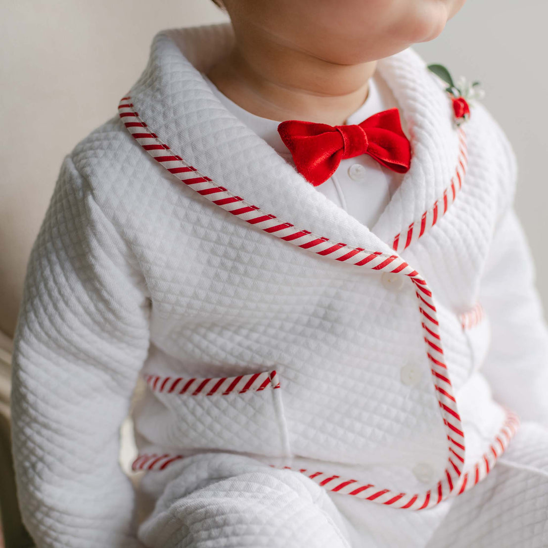 Child wearing a white outfit with red trim and a red bow tie against a neutral background