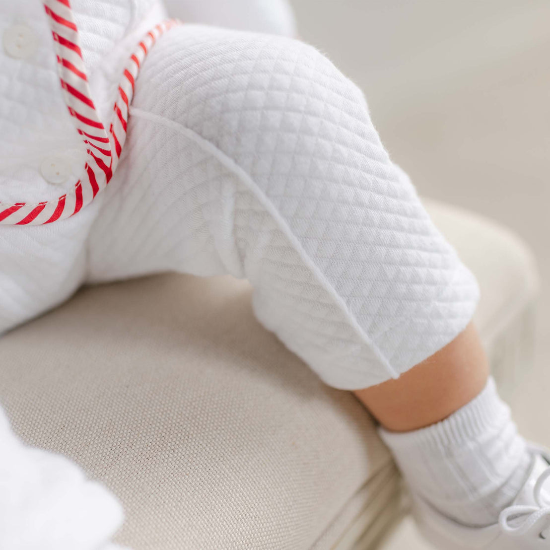 Person wearing white sneakers and light-colored pants sitting on a beige surface.