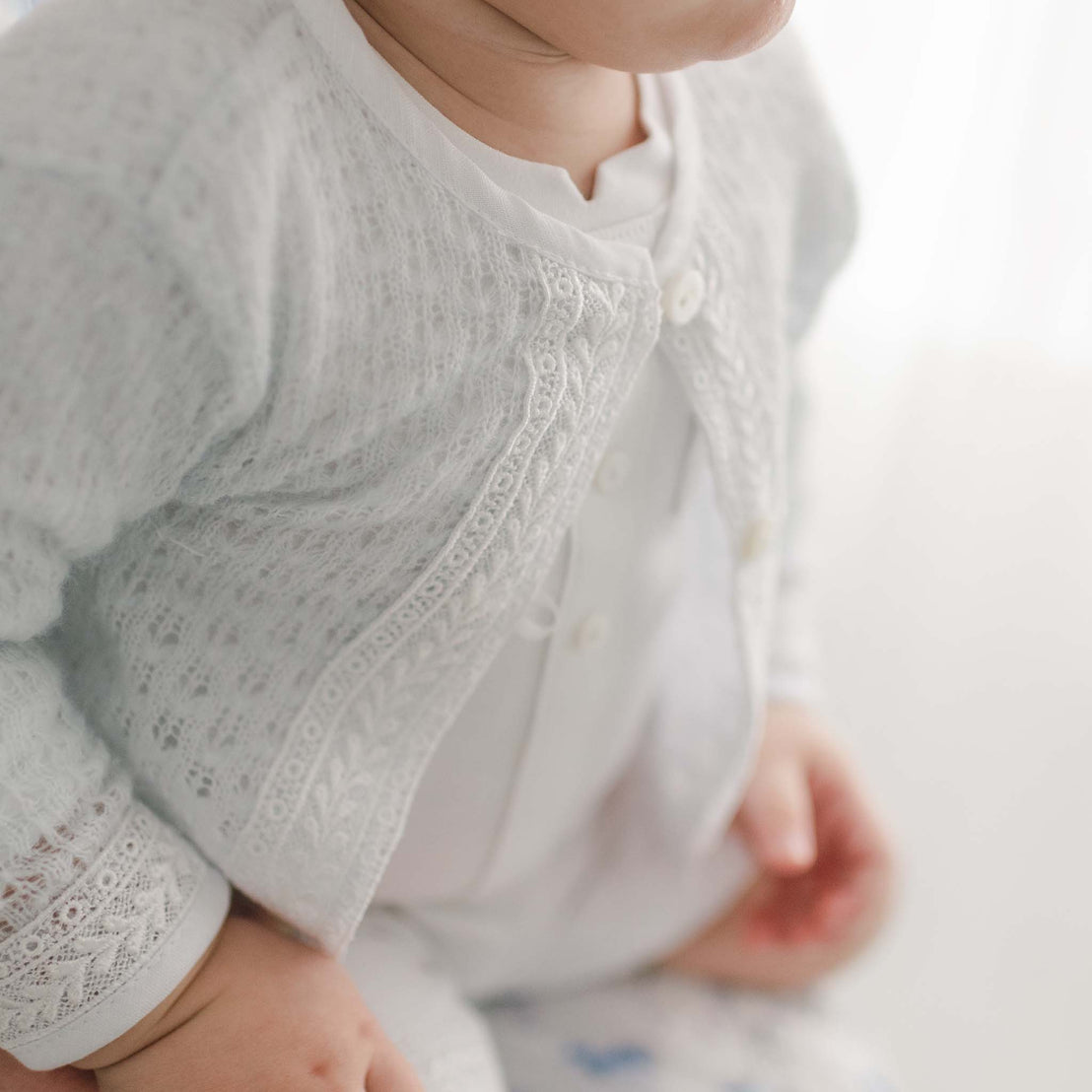 Close-up of a baby boy wearing the light blue Oliver Sweater Shorts Suit with white Venice lace trim, focusing on the details of the clothing and the baby's folded hands.