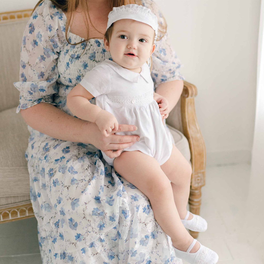 Smiling baby boy sitting on mom's lap and wearing the Oliver Bubble Romper (and matching Oliver Linen Cap and Oliver Linen Booties).