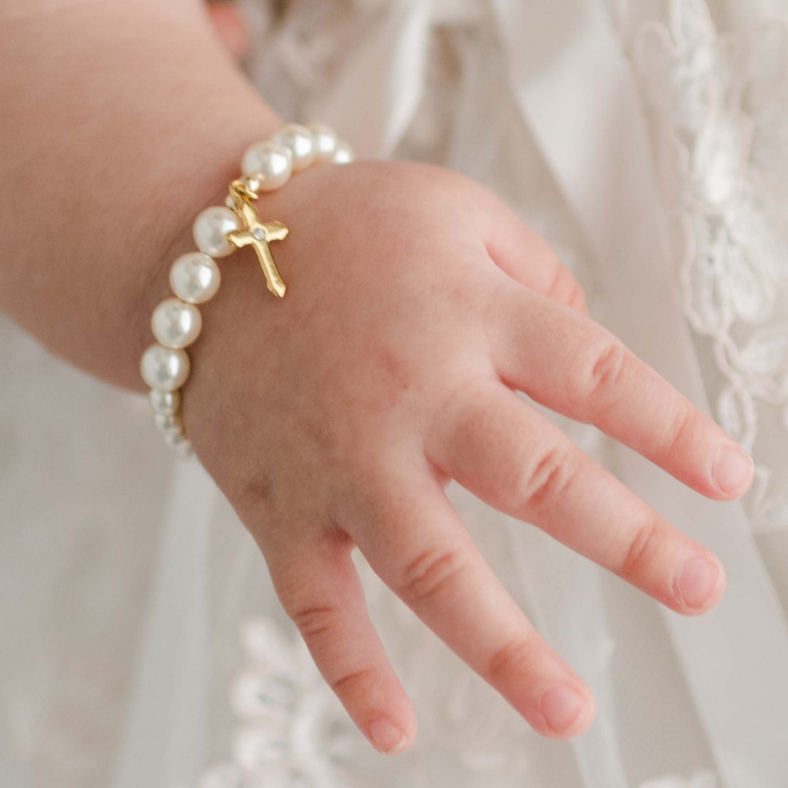 Close detail of Cream Luster Pearl Bracelet with Gold Cross on a baby girl's wrist.