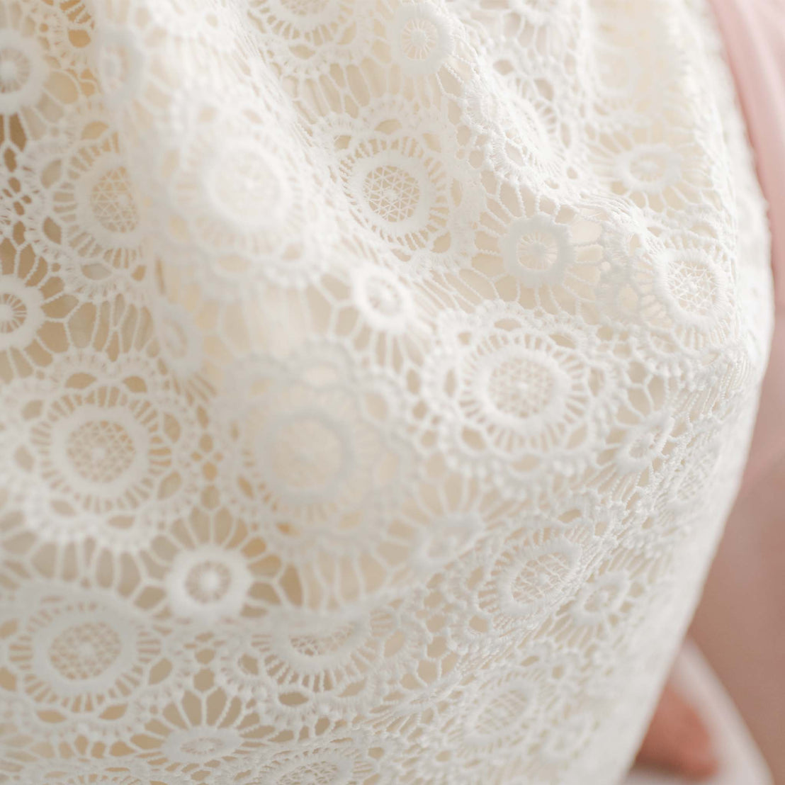 Close-up of a white lace fabric with intricate circular patterns, reminiscent of a delicate Poppy Christening Gown & Bonnet. The fabric, handmade in the USA, seems to be draped over a surface.